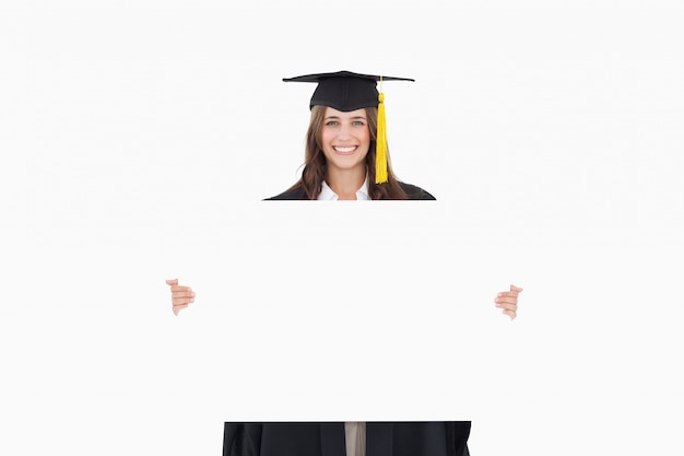 Una mujer en su toga de graduación tiene una hoja en blanco frente a ella