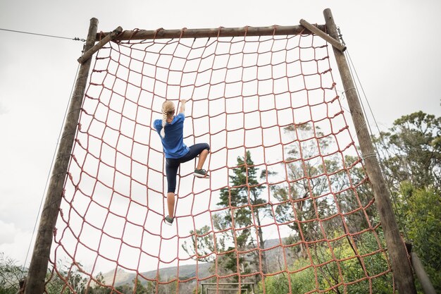 Mujer subiendo una red durante la carrera de obstáculos en el campo de entrenamiento