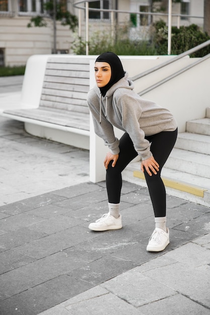 Una mujer con una sudadera con capucha gris está haciendo sentadillas en la acera.