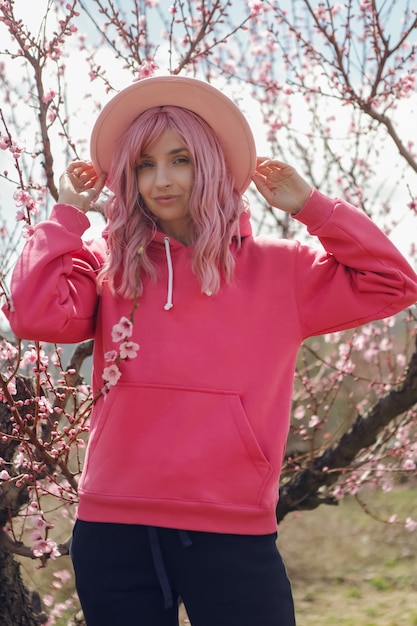 Mujer con una sudadera con capucha rosa y una peluca de pelo se encuentra en un campo de duraznos con flores en primavera en Crimea