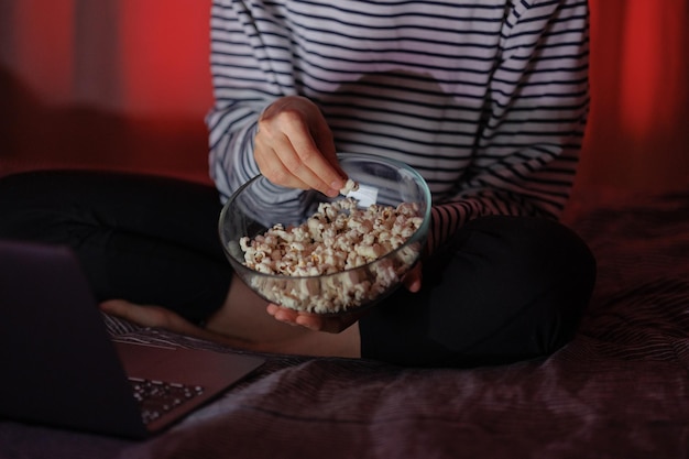 Foto mujer con una sudadera a rayas y sombrero come palomitas de maíz y ve una película en la televisión o una serie de televisión en