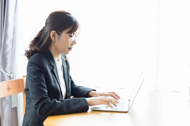 Una mujer del sudeste asiático con traje y escribiendo documentos en su computadora portátil