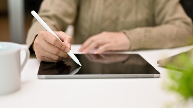 Mujer en un suéter acogedor usando lápiz óptico dibujando o escribiendo en la pantalla de la tableta usando una tableta digital