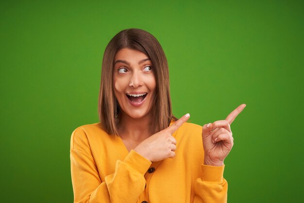 Foto mujer en suéter amarillo pensando y apuntando sobre fondo verde