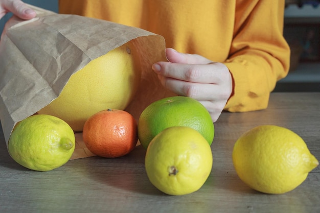 Una mujer con un suéter amarillo saca una fruta de colores brillantes de un primer plano de una bolsa de papel