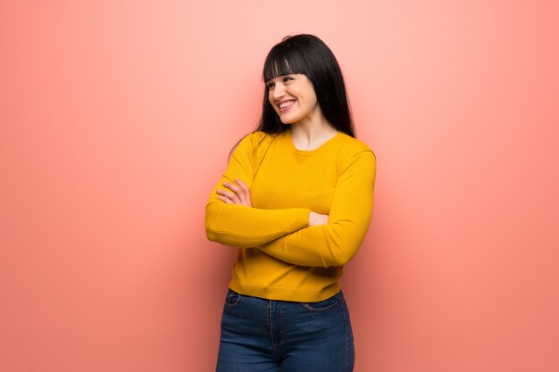 Mujer con suéter amarillo sobre pared rosa Feliz y sonriente