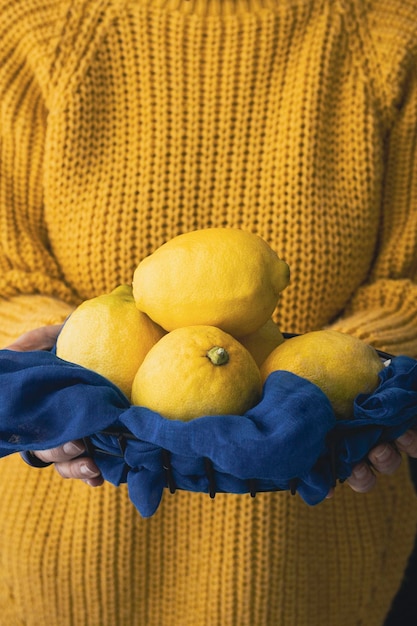 Mujer con suéter amarillo sosteniendo algunos limones frescos