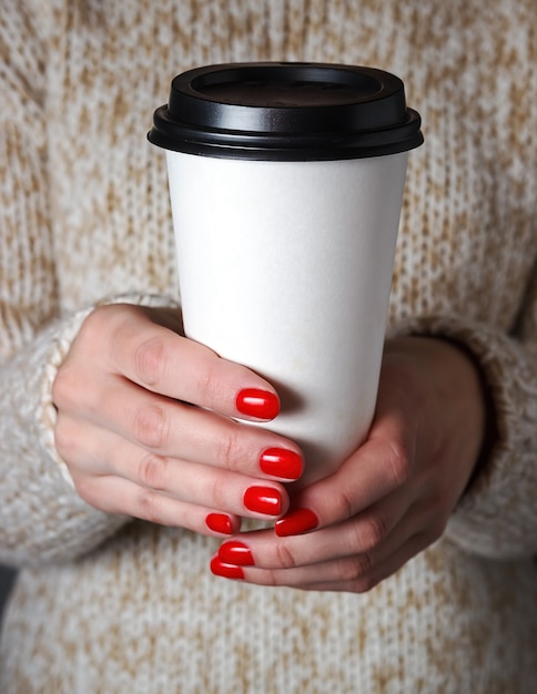 Mujer en un suéter beige sosteniendo una taza de café de papel