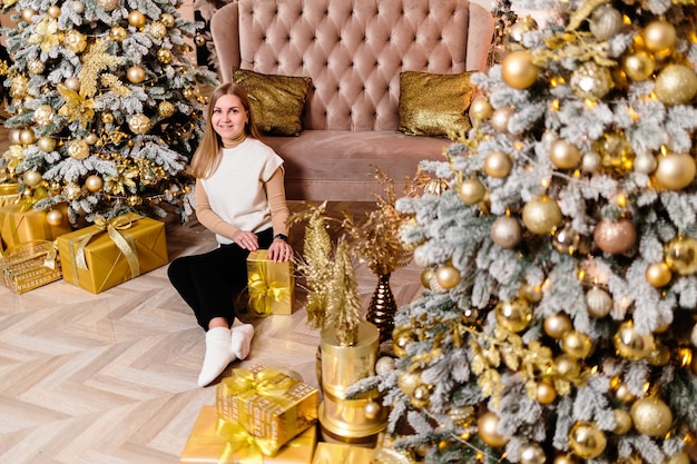 Mujer en suéter blanco cálido y acogedor por la noche en un interior de Navidad Árbol de Navidad decorado con guirnaldas de luces iluminando el interior Enfoque suave