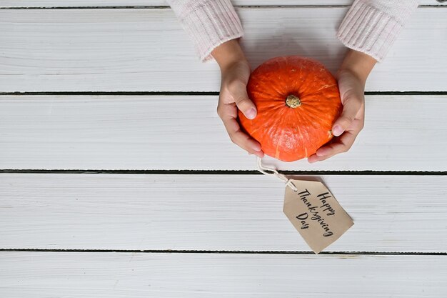 Mujer en suéter blanco cálido sostiene calabaza naranja madura sobre fondo blanco.