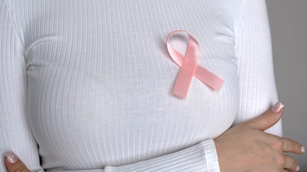 Una mujer con un suéter blanco con una mosca rosa en apoyo de pacientes con cáncer de mama