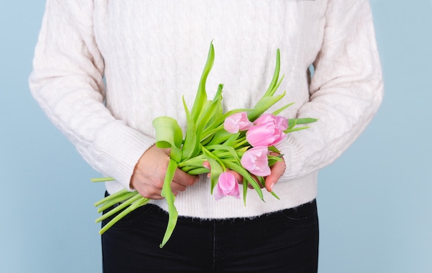 Mujer en un suéter blanco con un ramo de tulipanes rosados. Concepto de primavera.