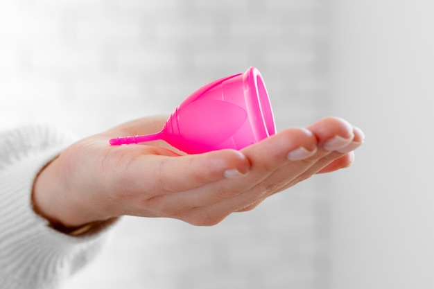 Foto mujer en suéter blanco sosteniendo la copa menstrual rosa en las manos de cerca