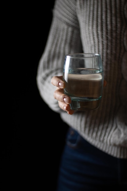 Una mujer con un suéter gris sostiene un vaso de agua limpia en la mano