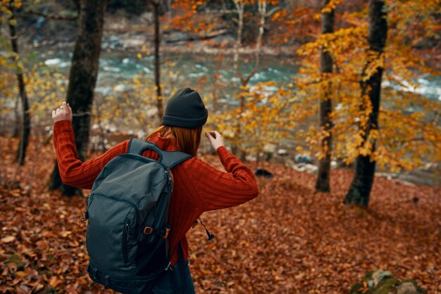 Foto mujer en un suéter con una mochila y en vaqueros camina a través del bosque de otoño en las montañas cerca del río foto de alta calidad