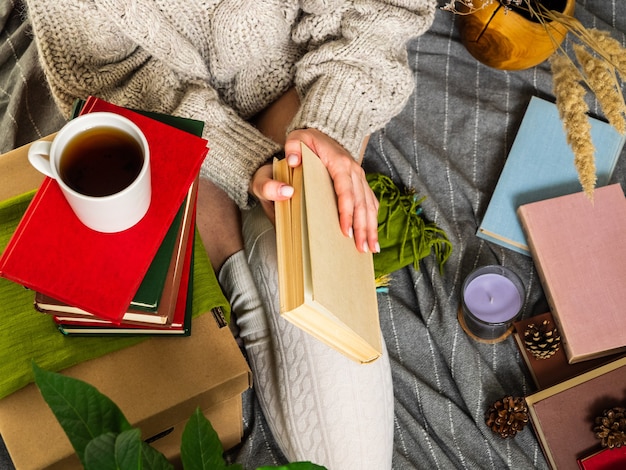 Mujer con un suéter de punto rodeado de muchos libros diferentes