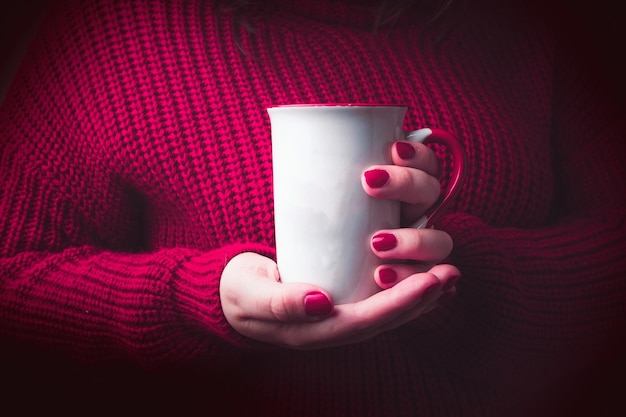 Mujer con suéter rojo acogedor sosteniendo taza blanca para maqueta.