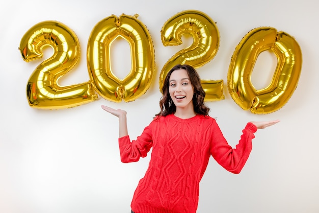 Mujer en suéter rojo apuntando a globos de año nuevo 2020