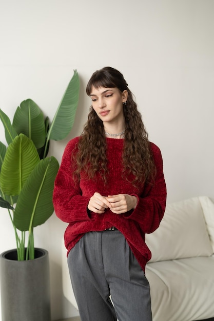 Una mujer con un suéter rojo se para frente a una planta.