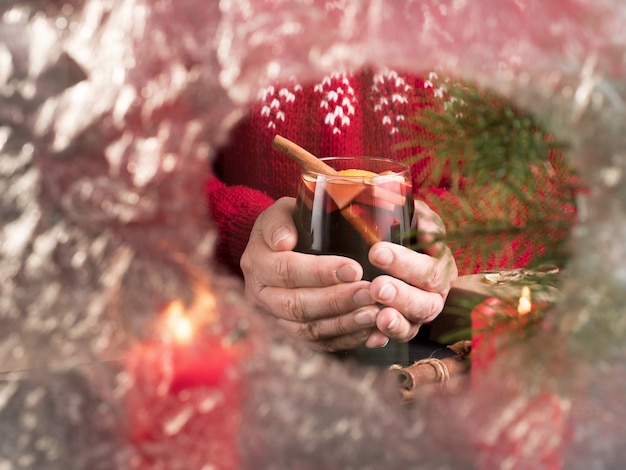 Una mujer con un suéter rojo sostiene una copa de vino caliente detrás de una copa congelada. Vacaciones navideñas.