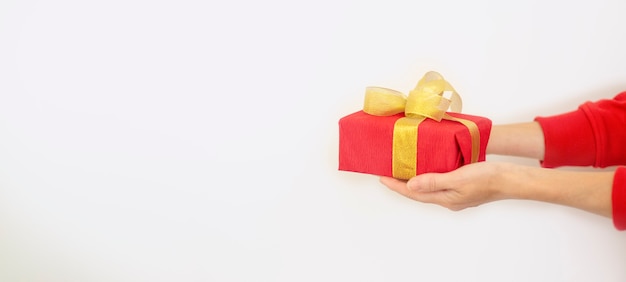 Una mujer con un suéter rojo sostiene un regalo de Navidad rojo sobre un fondo blanco. Concepto de regalo para Navidad y año nuevo.