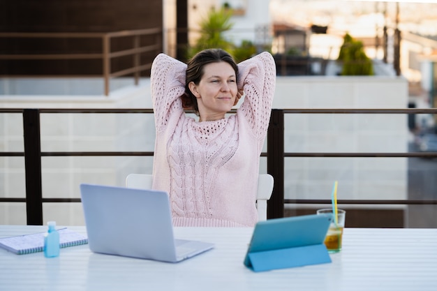 Mujer en suéter rosa casual relajado mientras trabajaba remotamente en la terraza de su casa