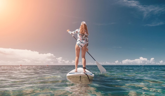 Mujer sup mar feliz mujer en forma saludable en bikini relajándose en una tabla de surf sup flotando en el claro