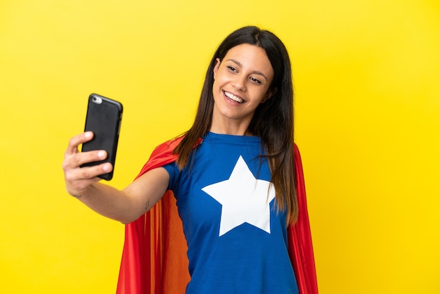 Mujer superhéroe aislada sobre fondo amarillo haciendo un selfie con teléfono móvil