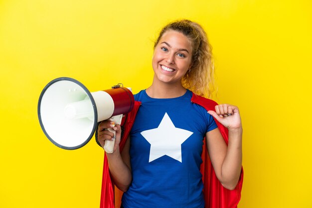 Mujer superhéroe aislada sobre fondo amarillo sosteniendo un megáfono y orgullosa y satisfecha de sí misma