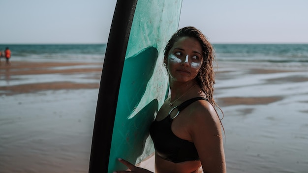 Mujer surfista europea con protector solar en la cara sosteniendo su tabla de surf