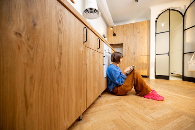 Mujer con una tableta digital sentada en el suelo de la cocina