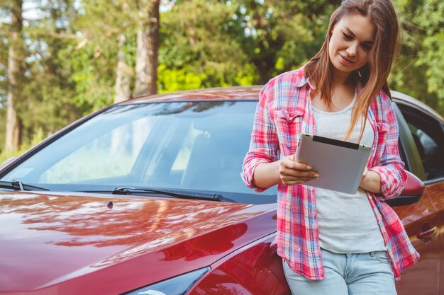 Mujer con una tableta en las manos de pie junto al coche