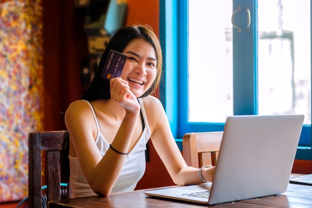 Mujer tailandesa bebiendo jugo de naranja en un café Usando laptop comprando en línea Trabajar con una computadora en una cafetería