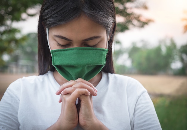 Mujer tailandesa que usa una máscara para proteger el virus, Covid 19 Orando por las bendiciones de Dios para que el mundo esté a salvo de esta epidemia.