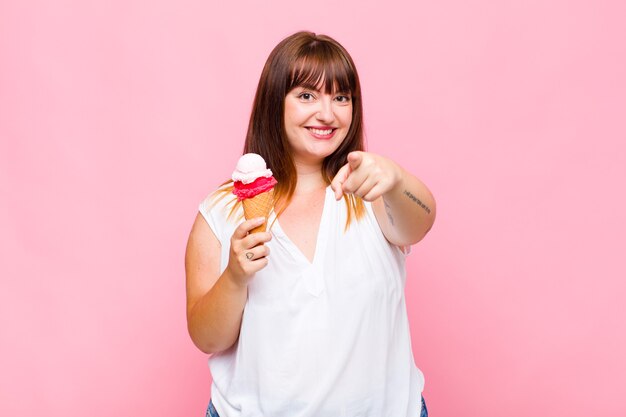 Mujer de talla grande apuntando a la cámara con una sonrisa satisfecha, confiada y amistosa, eligiéndote