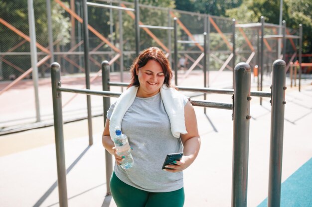 Una mujer de talla grande después de entrenar al aire libre encuentra alegría con su teléfono inteligente y su sonrisa irradia
