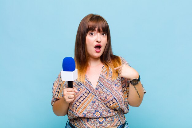 Mujer de talla grande mirando consternado y sorprendido con la boca abierta, apuntando a sí mismo