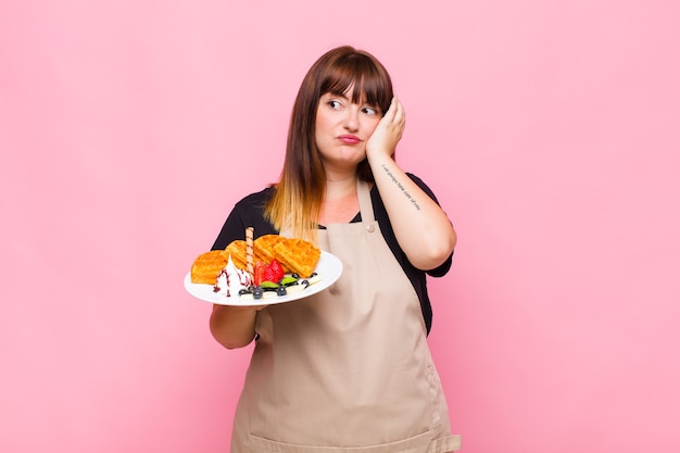 Mujer de talla grande que se siente aburrida, frustrada y con sueño después de una tarea aburrida, aburrida y tediosa, sosteniendo la cara con la mano