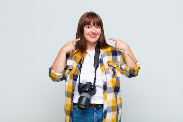 Foto mujer de talla grande sonriendo con confianza apuntando a su propia sonrisa amplia, actitud positiva, relajada y satisfecha