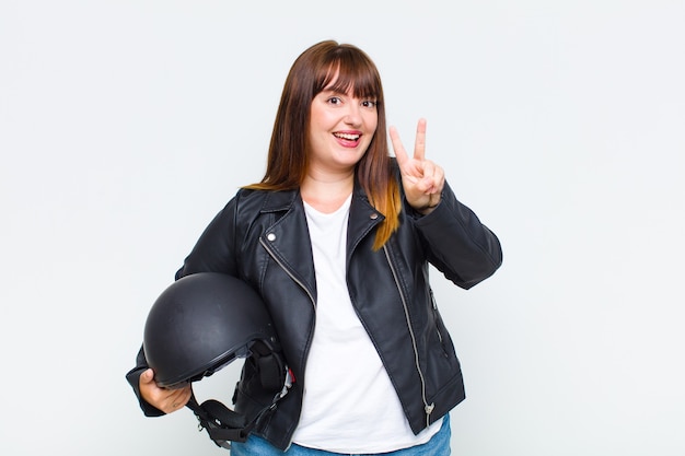 Mujer de talla grande sonriendo y luciendo feliz, despreocupada y positiva, gesticulando victoria o paz con una mano