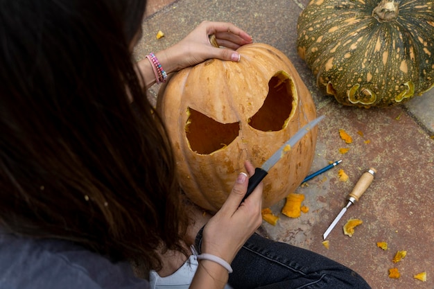 Mujer tallando una gran calabaza naranja para Halloween mientras se sienta en una mesa de madera en casa