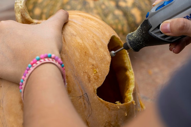 Mujer tallando una gran calabaza naranja para Halloween mientras se sienta en una mesa de madera en casa