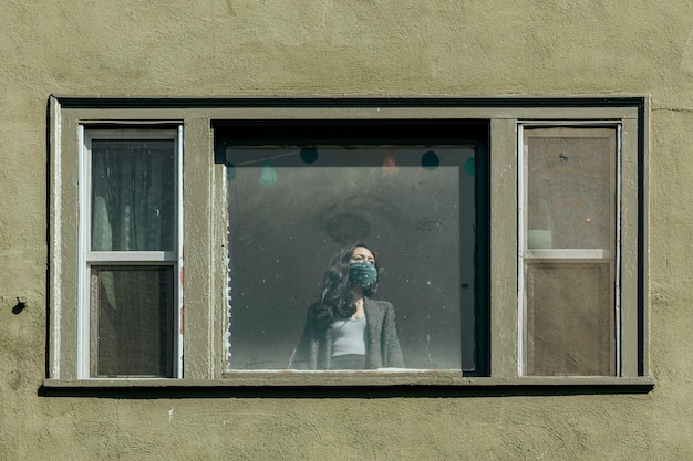 Mujer tapándose la boca con un pañuelo mirando por la ventana durante el encierro por coronavirus.