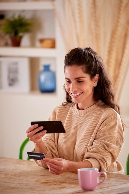 Mujer con tarjeta de crédito en casa usando teléfono móvil para revisar las finanzas para iniciar negocios