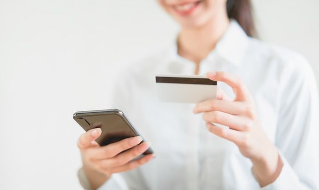 Mujer con tarjeta de crédito con compras en línea en el teléfono inteligente e ingrese el código de pago del producto en la oficina en casa.