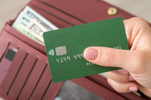 Mujer con tarjeta de crédito en las manos sobre el fondo del bolso con billetes de dólar Usando tarjeta de crédito de plástico o efectivo