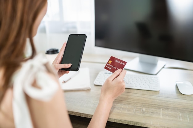 Mujer con tarjeta de crédito y usando el móvil para comprar en línea mujer asiática que trabaja en casa Compras en línea comercio electrónico banca por Internet gastar dinero trabajando desde el concepto de hogar