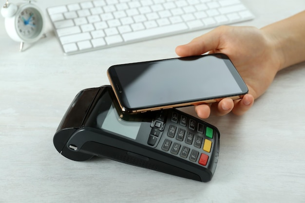 Mujer con tarjeta de crédito usando terminal de pago moderno en el primer plano de la mesa blanca