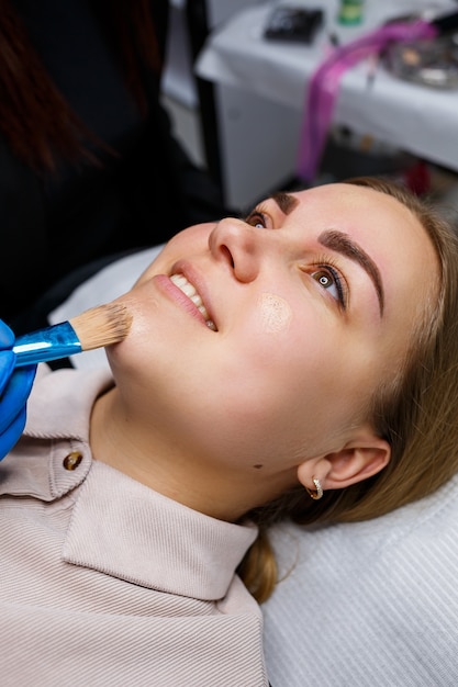 Mujer con tatuaje de maquillaje permanente en las cejas. Esteticista de primer plano hace que el maquillaje aplique una base. Maquillaje profesional y cuidado cosmético de la piel.