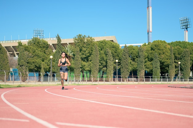 Mujer con tatuajes corriendo en pista atlética en un día soleado